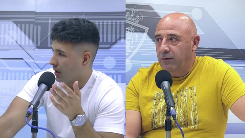 Dos hombres sentados frente a micrófonos en un estudio con fondo azul y gris, uno de camiseta blanca y otro de camiseta amarilla.