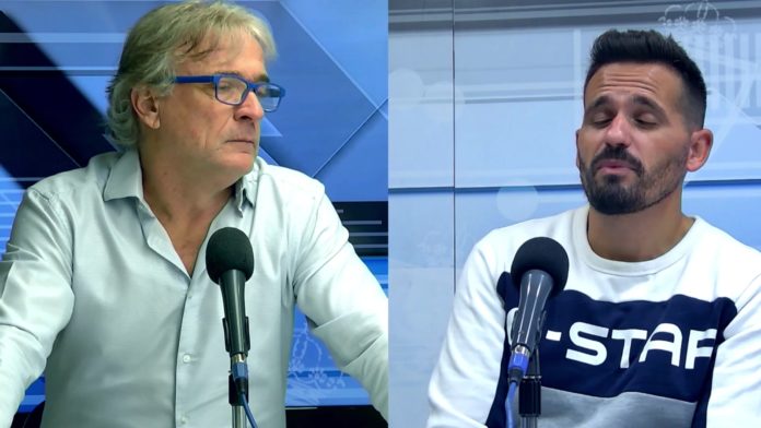 Dos hombres sentados separados por una división, cada uno frente a un micrófono, en un estudio con fondo azul.